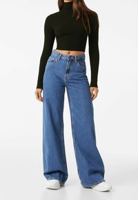 High-waisted, wide-leg jeans in blue denim, featuring a classic five-pocket design and visible stitching. Paired with a black ribbed crop top.