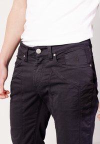 Vaqueros negros de algodón con ajuste slim, bolsillos delanteros con costuras únicas y un botón de metal pulido en la cinturilla.