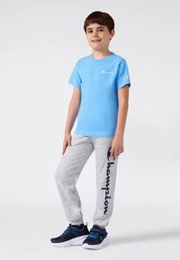 Lyseblå kortermet t-skjorte med hvit logo, kombinert med grå joggebukser med svart "Champion"-tekst, og marineblå sportsko.