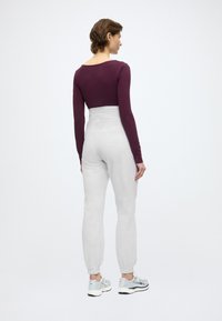 Μπλούζα μακρυμάνικη σε βαθύ μωβ χρώμα, συνδυασμένη με ψηλόμεσα ανοιχτό γκρι παντελόνια φόρμας με ελαστικές μανσέτες. Το μοντέλο φοράει λευκά και γκρι αθλητικά παπούτσια.