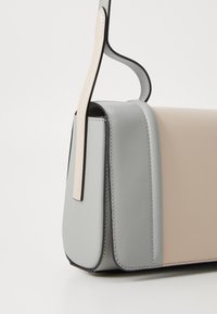 Borsa rettangolare realizzata in pelle liscia di colore grigio chiaro e beige, con un bordo nero a contrasto e una tracolla piatta attaccata nella parte superiore.