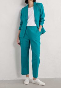 Turkusowy garnitur z dopasowaną marynarką i spodenkami 7/8, w połączeniu z białym t-shirtem i białymi trampkami. Gładka tkanina, minimalistyczny design.