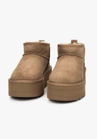 Beżowe zamszowe botki za kostkę z grubą platformą, z miękką podszewką i minimalnymi przeszyciami. Prosty, zaokrąglony kształt z pętelką do ściągania.