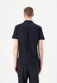 Camicia a maniche corte in tessuto strutturato color navy. Presenta un colletto rigido e una cucitura sul retro per una vestibilità su misura.
