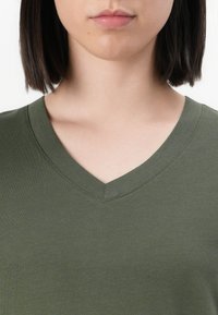 T-shirt verde oliva a maniche corte con scollatura a V, dalla texture liscia, caratterizzato da un design semplice e classico e cuciture rinforzate.