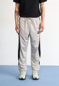 Ljusgrå träningsbyxor med svarta sidopaneler, elastisk midja med dragsko och logopatch. Bärs med grå och svarta sneakers.