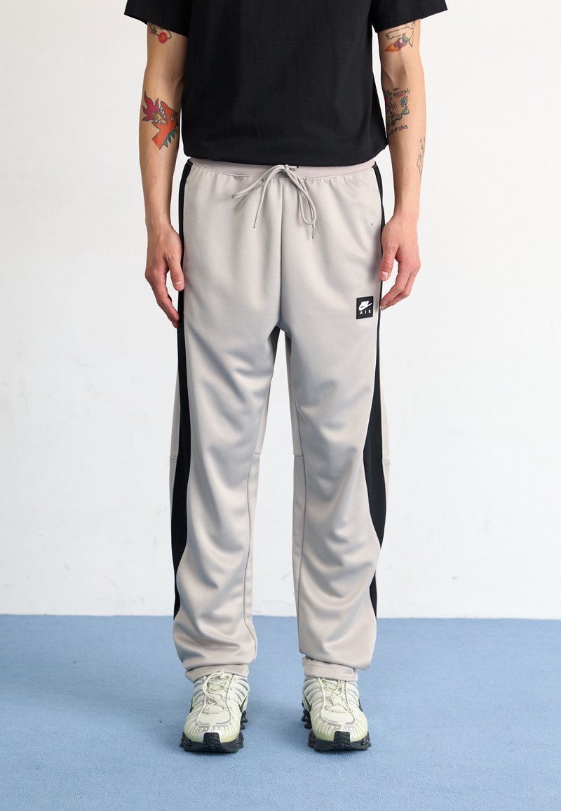 Ljusgrå träningsbyxor med svarta sidopaneler, elastisk midja med dragsko och logopatch. Bärs med grå och svarta sneakers.