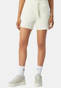 Witte katoenen shorts met een elastische tailleband en een trekkoord. Heeft een losse pasvorm, korte lengte en is gecombineerd met lichtgrijze sneakers en witte sokken.