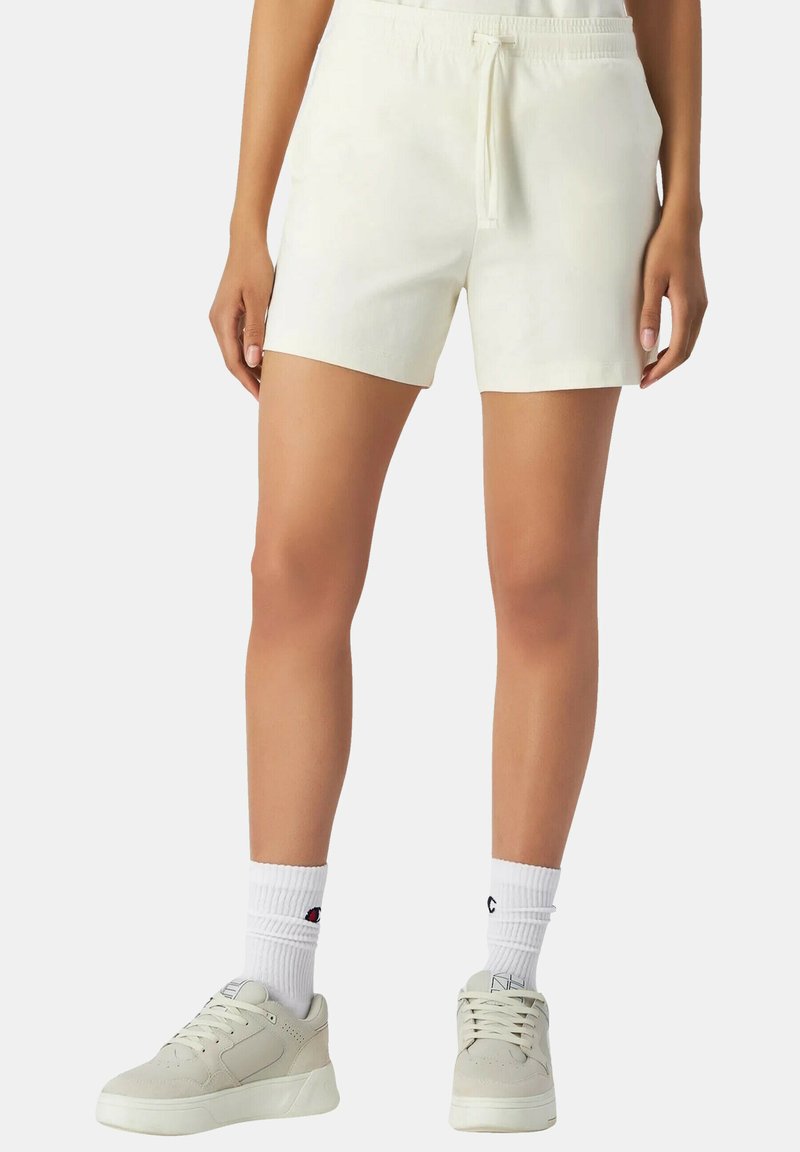 Witte katoenen shorts met een elastische tailleband en een trekkoord. Heeft een losse pasvorm, korte lengte en is gecombineerd met lichtgrijze sneakers en witte sokken.