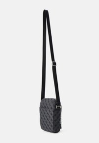 Bolso bandolera de tela gris con patrón de logo negro. Cuenta con una correa negra y un cierre de cremallera, con una forma rectangular compacta.