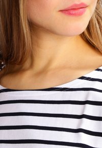 Witte shirt met horizontale zwarte strepen, brede halslijn en zachte textuur. Bevat een gladde huid en natuurlijke lipkleur.