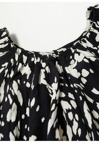 Blouse à motifs noir et blanc avec un col froncé. Le tissu est léger et texturé, avec des formes abstraites aléatoires partout.