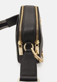 Schwarze Leder-Umhängetasche mit doppelten goldenen Reißverschlüssen, einem abnehmbaren Kettenriemen und einer strukturierten Außenseite. Mit goldenen Hardware-Akzenten.