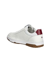 Witte sneaker met een bovenwerk van textuurstof, een bruine rubberen zool en een rood accent op de hiel. Heeft een lage snit en een veterafsluiting.