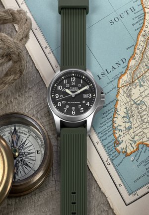 Zegarek Timex Expedition z srebrową kopertą, czarną tarczą, białymi cyframi i zielonym gumowym paskiem. Zasilany energią słoneczną z wyświetlaczem daty, teksturowany pasek.
