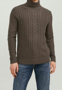 Brązowy sweter z dzianiny z wysokim kołnierzem, wzorem w warkocze, ściągaczami na mankietach i u dołu, w połączeniu z niebieskimi dżinsami.