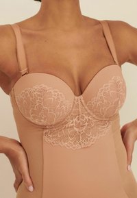 Body nude avec des détails en dentelle au niveau de la poitrine, bonnets rembourrés, bretelles réglables et une texture lisse. Le design offre un soutien et une couverture.