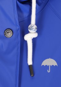 Zils ūdensizturīgs jaka ar baltu auklu un dekoratīvu pērlīti, ar burāšanas kuģa dizainu. Sudraba lietussarga logo uz priekšpuses.