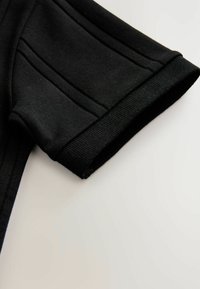 Indumento nero a maniche corte con orlo e dettagli di cucitura a coste, realizzato in un tessuto morbido e liscio con un design strutturato.