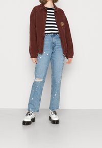 Vinröd flanelljacka, randig svart och vit skjorta, urtvättade ljusblå jeans med färgfläckar, och vita platåstövlar.