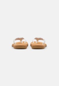 Hvite sandaler med teksturerte stropper, fleksible tan såler og et mønstret såle. Designet har åpen tå og er bakløs.