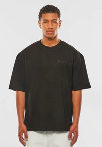 Sort oversized t-shirt lavet af bomuld, med korte ærmer og rund halsudskæring. Diskret præget "Dropsize" branding på brystet.