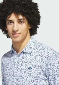 Kortærmet skjorte i lyseblåt stof med et bladmønster i marineblå og pink. Har krave og en lille logo på venstre bryst.