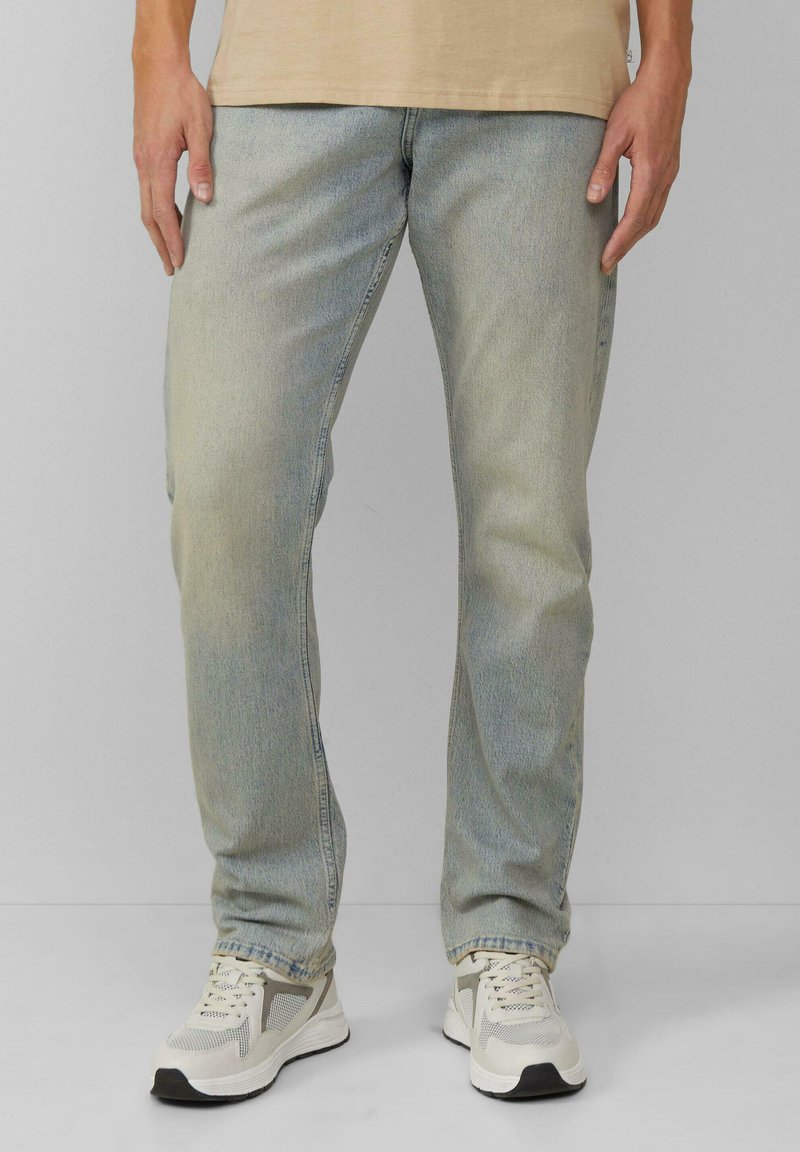 Jasnoniebieskie dżinsy o prostym kroju, z delikatnym wyblaknięciem i klasycznym pięcio-kieszeniowym designem, zestawione z neutralnymi trampkami.