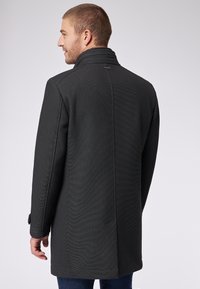 Dunkelgrauer Mantel aus strukturiertem Stoff, mit hohem Kragen, taillierter Passform und geknöpften Manschetten. Minimalistisches Design mit klaren Linien.