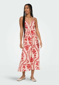 Robe maxi avec un motif floral rouge sur un fond clair, décolleté en V, bretelles réglables et une silhouette fluide ; assortie à des chaussures plates.