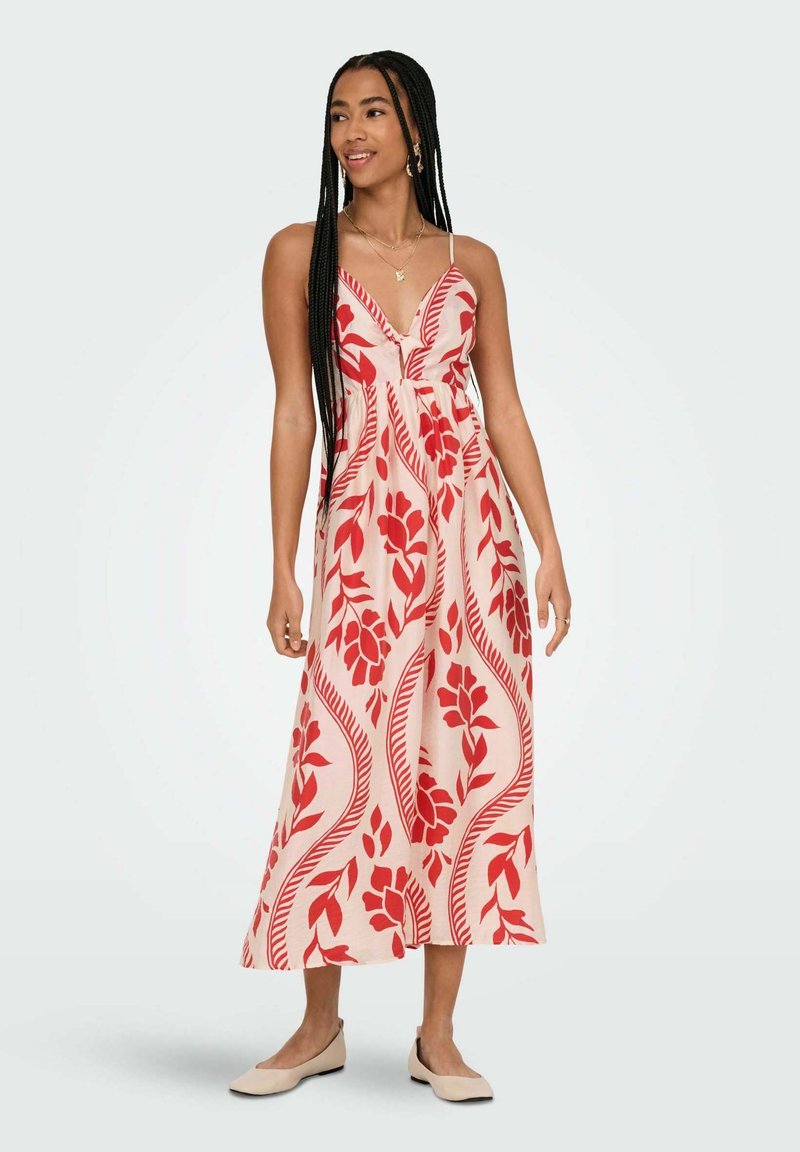 Robe maxi avec un motif floral rouge sur un fond clair, décolleté en V, bretelles réglables et une silhouette fluide ; assortie à des chaussures plates.