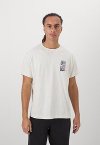 Cremefarbener Baumwoll-T-Shirt mit rundem Halsausschnitt, kurzen Ärmeln und einem Druck auf der Vorderseite mit dem Text "FIND YOUR FINE" in fetter schwarzer und pinker Schrift.