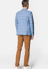 Jasnoniebieska marynarka w kratę o znormalizowanym kroju, w połączeniu z brązowymi spodniami. Całość charakteryzuje nowoczesny krój i casualowe białe trampki.