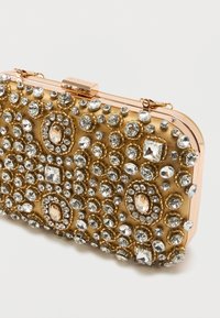 Obdélníková zlatá večerní kabelka zdobená různě tvarovanými průhlednými kamínky a s rámovým uzávěrem z růžového zlata.