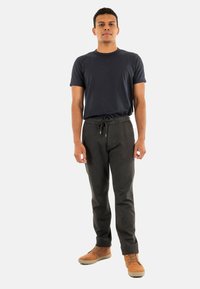 T-shirt a girocollo blu scuro abbinato a pantaloni della tuta grigi con coulisse. Il modello indossa scarpe marroni con lacci, in piedi su uno sfondo bianco semplice.