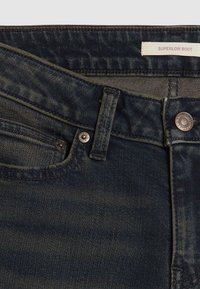 Tummansiniset farkut, joissa on erittäin matala boot cut, näyttävällä ompelulla, metallinappi kiinnityksessä ja hienovaraisella tekstuurilla.