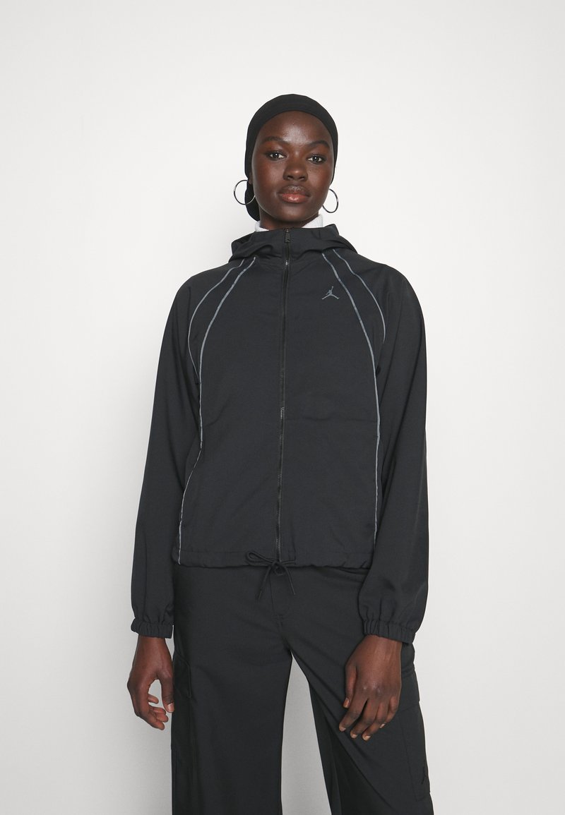 Chaqueta ligera negra con cremallera y capucha, con costuras grises, dobladillo con cordón y el logo de Jordan en el pecho. Textura suave.