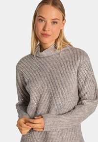 Grijs gebreid sweater met een ribbelstructuur, voorzien van glanzende, ingeweven pailletten. Hoge, opgerolde kraag en lange mouwen met een relaxte pasvorm.