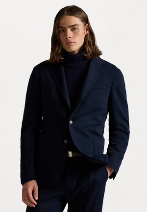 Marinblå blazer med slag, enkel knapp, strukturerad tyg och framfickor; ihop med en ribbad marinblå polotröja.