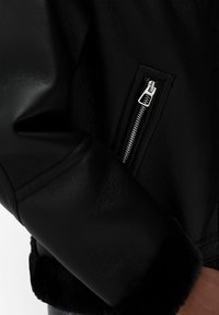 Zwarte leren jas met een ritssluiting op de zak en zachte zwarte bontafwerking bij de manchetten. Soepele textuur met een gestructureerde pasvorm.