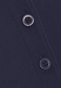 Primo piano di due bottoni blu navy scuro cuciti su un tessuto blu navy testurizzato con cuciture visibili e una cucitura che corre in verticale.