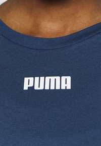 Blå t-shirt med vit fet "PUMA"-logotyp centrerad under halsringen på en persons övre bröst.