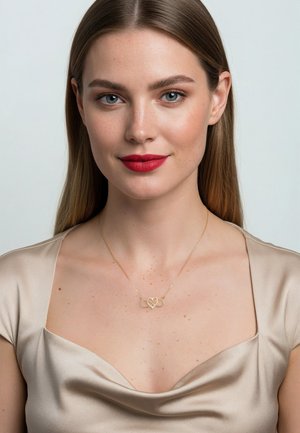 Guldhalskæde med sammenflettet hjerte- og uendelighedssymbol-design. Glat, skinnende finish. Bæres af en model med langt hår og en lysefarvet satin top.