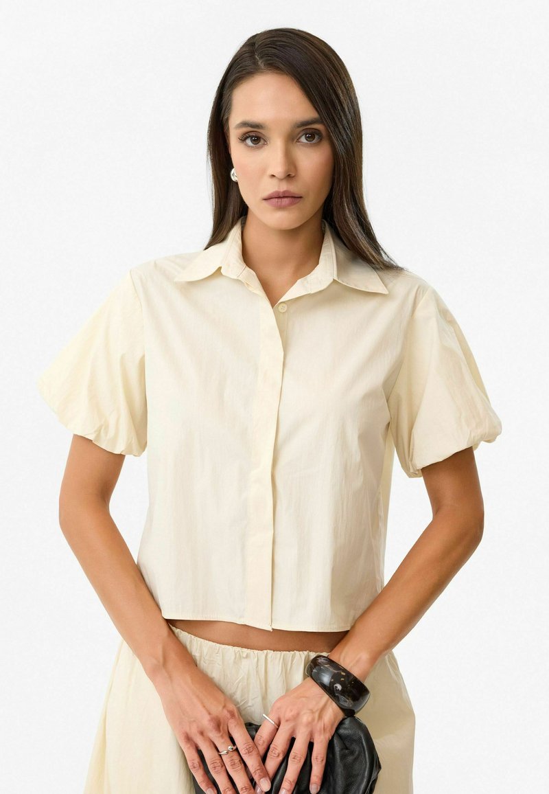 Korte mouw, cropped blouse in lichtgeel, met een knoopsluiting aan de voorkant, kraag en zachte, lichte stof.