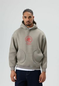 Sweat à capuche gris clair avec une grande poche avant, arborant un motif graphique circulaire rouge avec une rose. Tissu doux, coupe ample et design à capuche.
