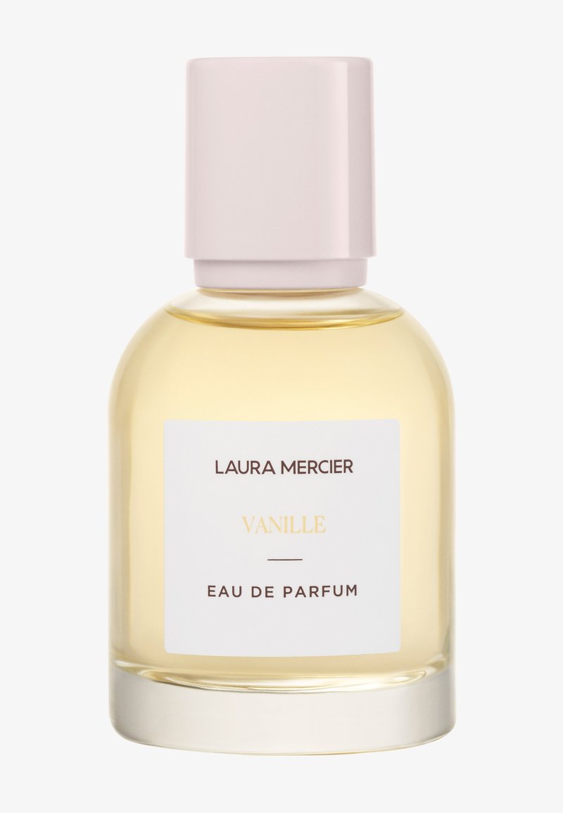 Bouteille de parfum en verre transparent avec une base ronde, liquide jaune clair et un capuchon rose pâle. Étiquette blanche avec texte foncé.