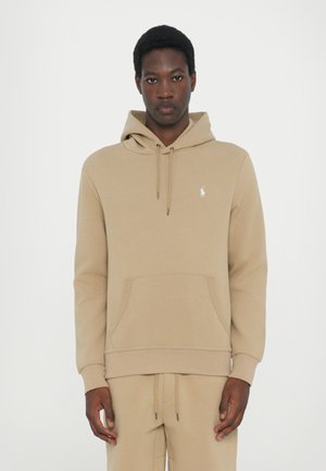 Beige pullover hættetrøje med en frontlomme, justerbar snøre i hætten og lille hvidt logo på brystet. Blødt, tekstureret stof.