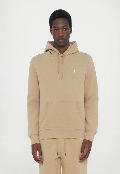 Beige hoodie made of soft fabric, featuring a kangaroo pocket, drawstring hood, and a small logo on the chest. Smooth texture throughout.