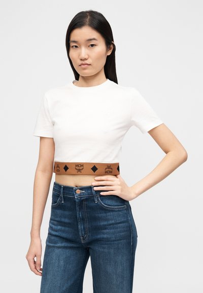 Λευκό κοντομάνικο μπλουζάκι με στρογγυλή λαιμόκοψη και ανάγλυφο λογότυπο, συνδυασμένο με ψηλόμεσα σκούρα μπλε τζιν παντελόνια με κούμπωμα κουμπιού.