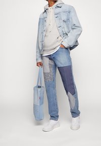 Light blue denim jacket, gray hooded sweatshirt, patchwork denim pants with floral and textured patches, light blue tote bag, white sneakers.